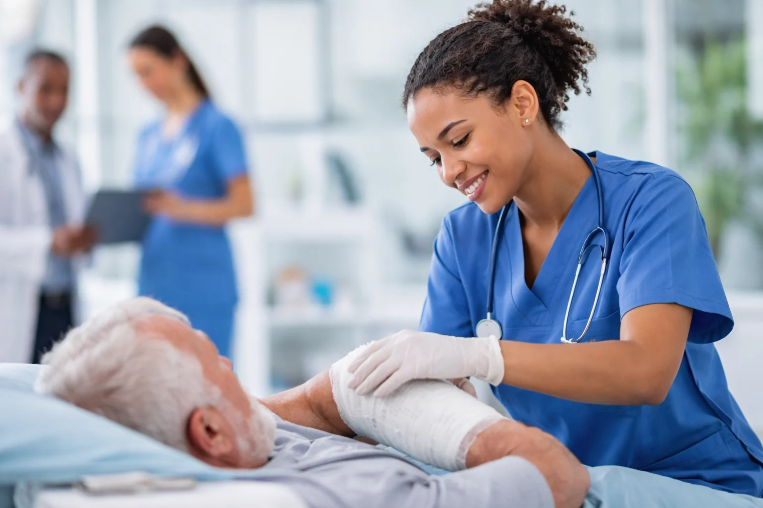 "A nurse in blue scrubs caring for an elderly patient’s arm wound, smiling while applying a bandage in a modern hospital setting, with healthcare staff in the background."