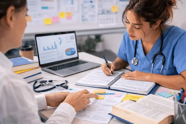 Nursing student in scrubs reviewing healthcare research notes with academic mentor while working on a nursing dissertation.