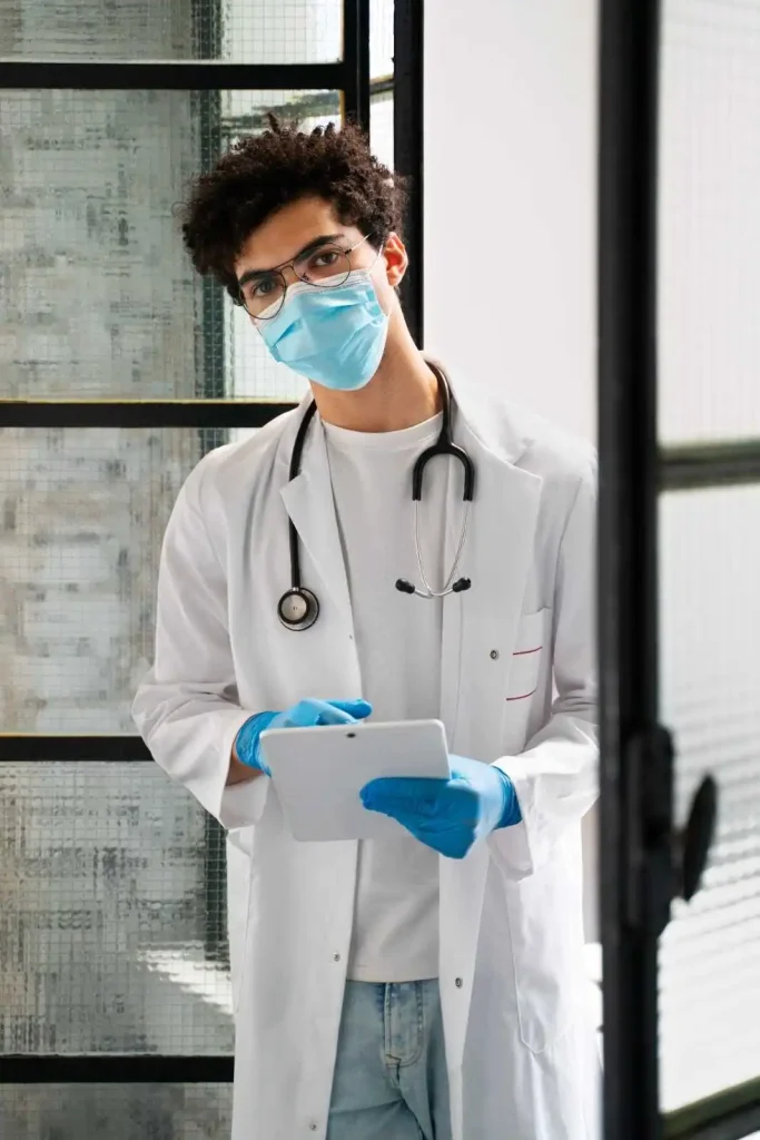 Healthcare professional wearing a face mask and gloves using a tablet in a modern medical facility.